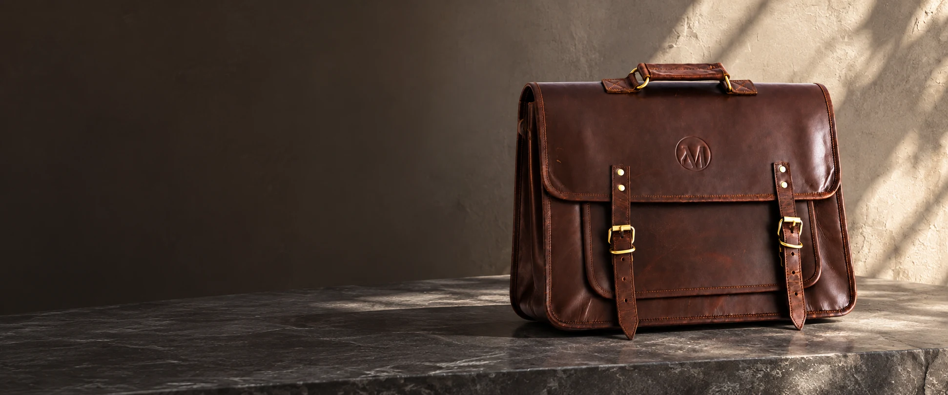 Compact Twin-Buckle Leather Messenger Bag displayed on a slate console beside a textured plaster wall